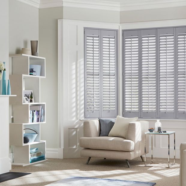 Grey tracked shutters fitted to a bay window in a living room