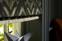 A dark green and black Roman blind finished in the Abigail Ahern Harkness Gasoline fabric. The blind has Colette Celeste fringing at the bottom