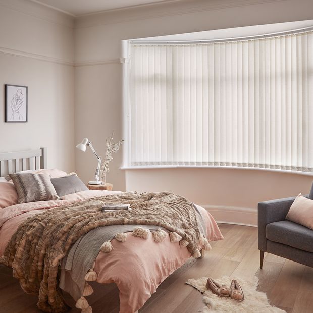Minimal luxe bedroom with soft furnishings and a bow window dressed with light cream vertical blinds