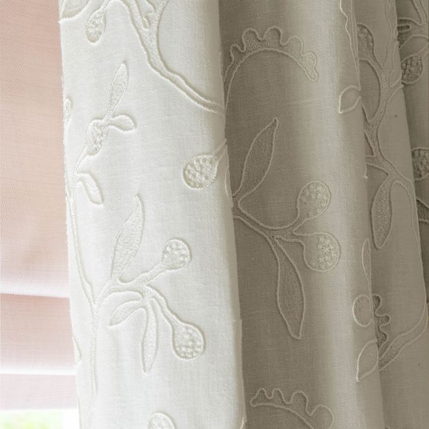 close up cream curtains featuring delicate embroidery hanging on bedroom window