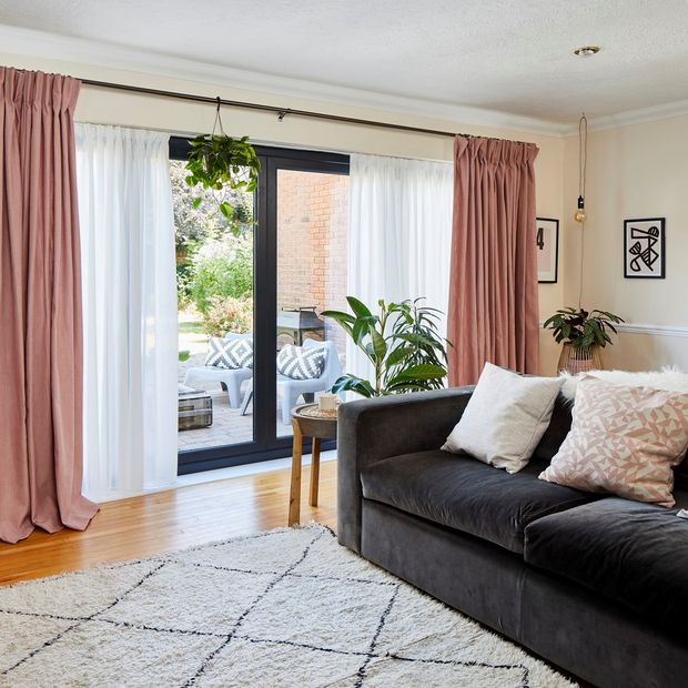 A living room with large bi fold doors dressed with pink curtains and white voiles