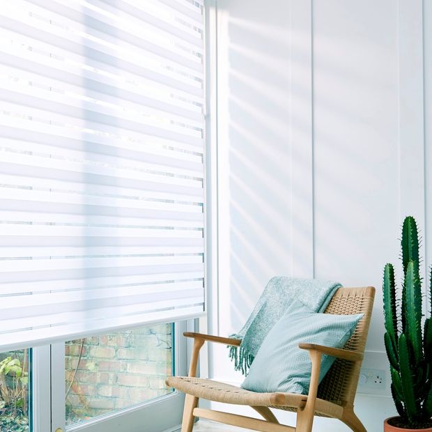 A close up of a white Day & Night blind in a room covering a wide window