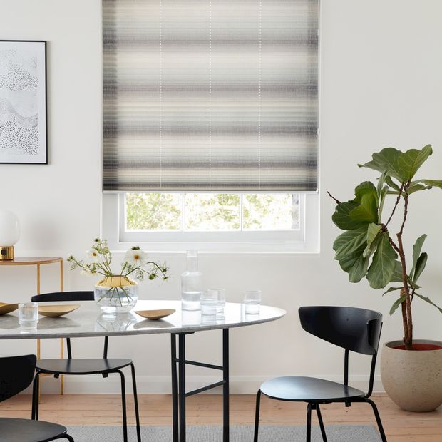 Mini stripe grey Pleated blinds from House Beautiful range hanging on single window in dining room. Grey dining table along with dark grey chairs is placed in room.