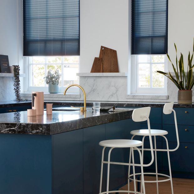Blue Pleated blinds dressed on windows of kitchen. Blinds are matching colour to cupboards and drawers of kitchen.