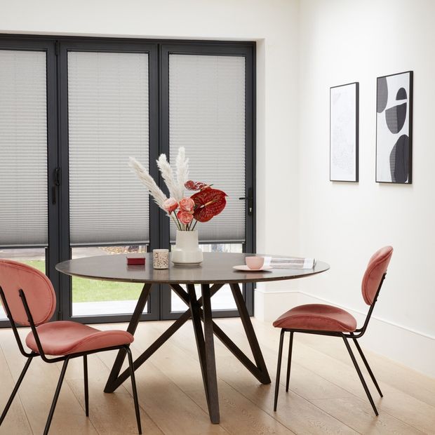 Grey Micro Pleat Pleated blinds dressed on bi-fold doors of dining room. Round table along with pink chairs have been placed in the room.