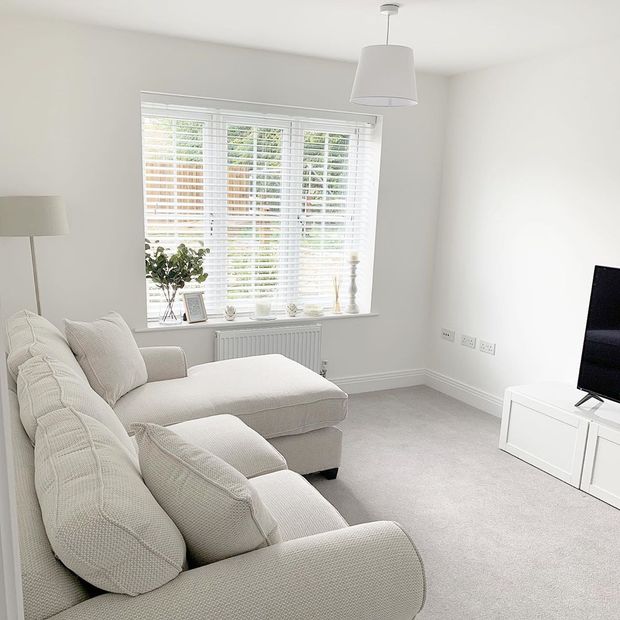 White wooden blinds hanging on the windows of white painted living room.  Cream sofa has been placed in the room.