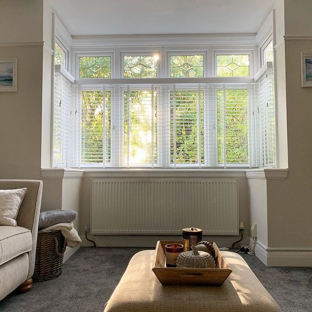 Living room with cream walls and sofas featuring bay window with white wooden veneitan blinds