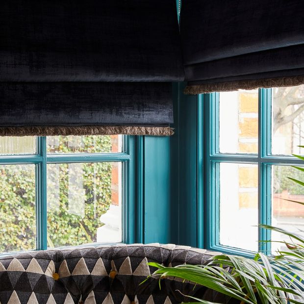 Black coloured roman blinds fitted to teal coloured windows in a room