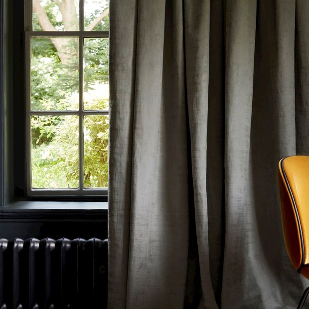 grey cley donkey curtains going down to floor infront of dark window ledge and radiator behind vibrant orange chair