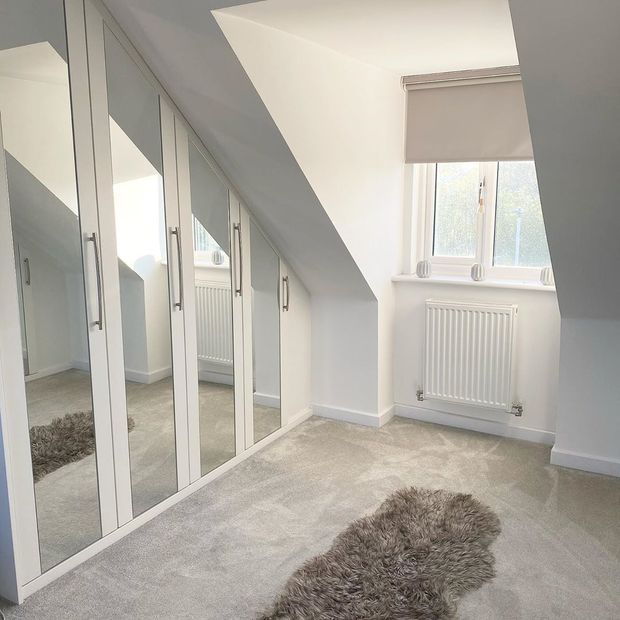 Roller blind in recessed window in slanted roof, fitted wardrobes with mirrors and fluffy rug