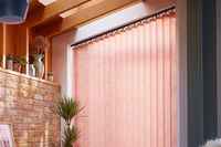 peach coloured vertical blinds fitted on a wide window in a living room with exposed brick work and wood slats