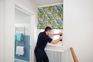 Someone installing a roman blind to a window on a landing