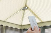 hand holding a remote infront of four motorised cream pleated blinds on a conservatory roof