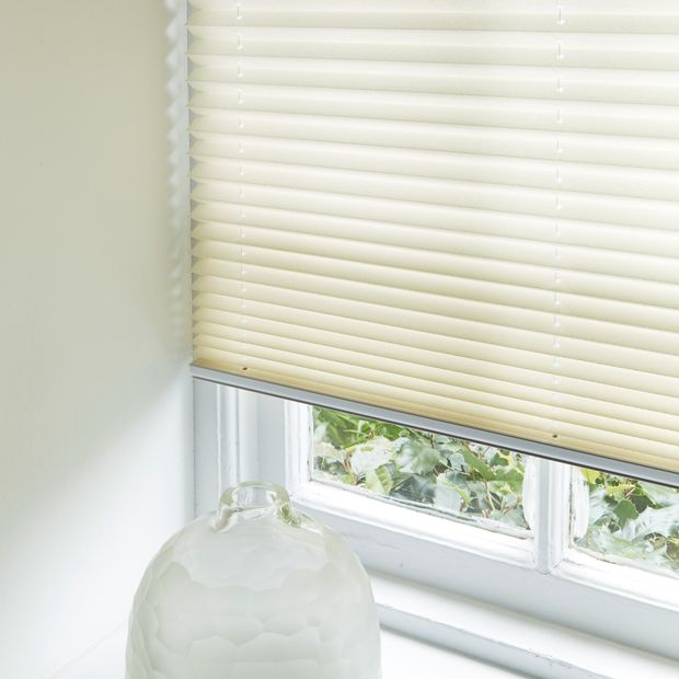 A cream coloured pleated blind fitted to a rectangular window on a white window sill