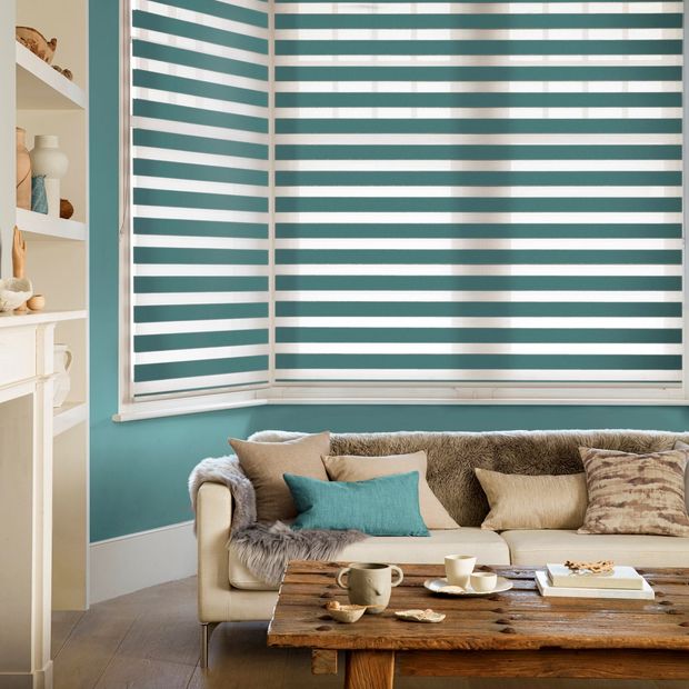 teal coloured striped blind with wooden table and beige sofa with matching teal cushion and fur throw