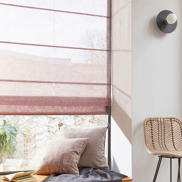 powder pink voile roman blindabove furnished window ledge next to a brown chair