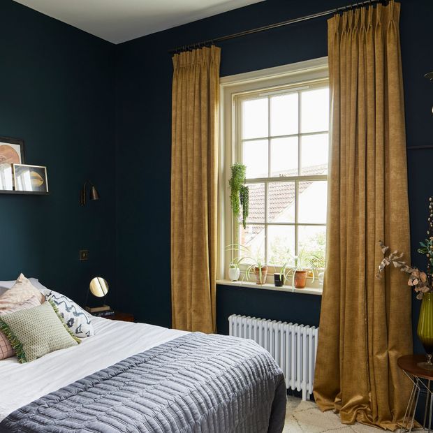 Mustard curtains in a bedroom. There is a bed on the left hand size that takes up the room. There is plotted plants in the room by the window and bed.