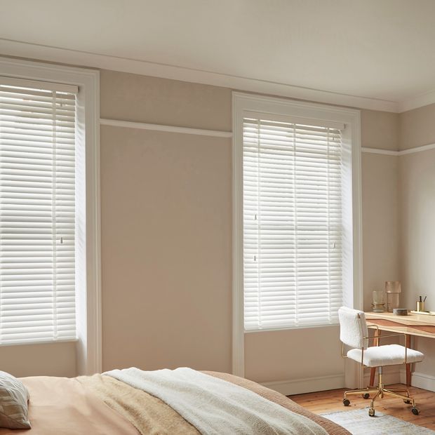 Ellwood Crystal White Wooden Blinds in a cream bedroom with a desk on he right side and a bed on the left.