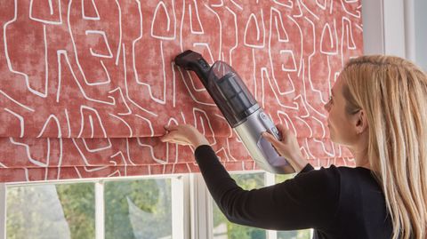 lady with blonde hair using a machine to clean a red roman blind with white patterns on it