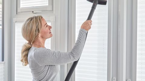 woman cleaning white pleated blinds with vacuum