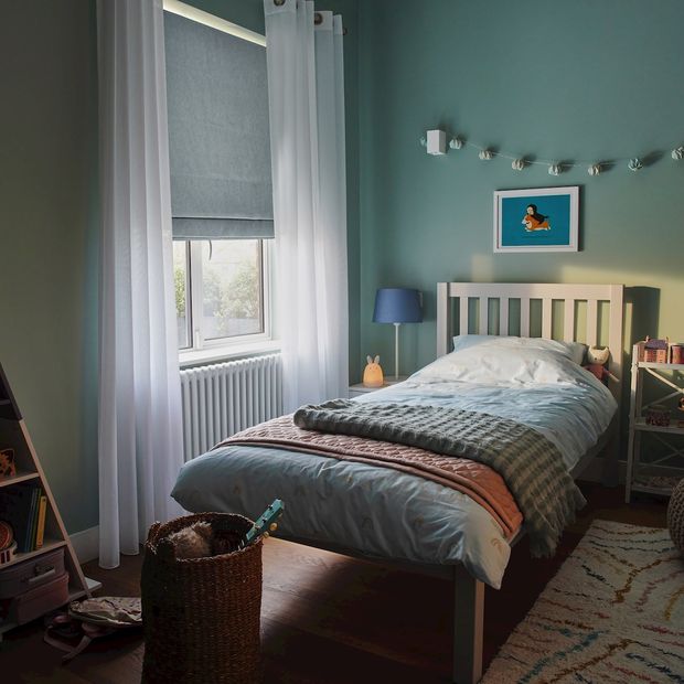 huxley powder blue roman blind beside a single bed in a childs bedroom with a bean bag, rug, and shelving for toys and books