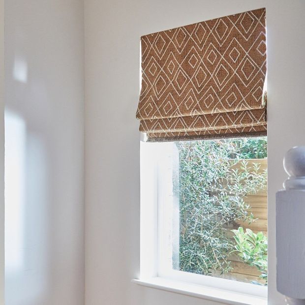Oriel sepia burnt orange diamond patterned roman blind on small window in hallway next to staircase