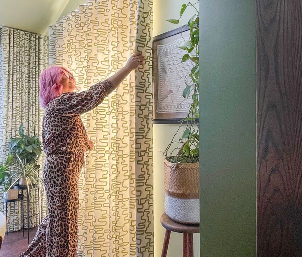 A-woman-in-leopard-print-pants-hangs-curtains-in-the-dining-room-of-Kiwi-Curtain