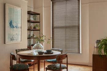 Neutral dining room with small round wooden table and chairs in front of window dressed in faux wood venetian blind fully extended