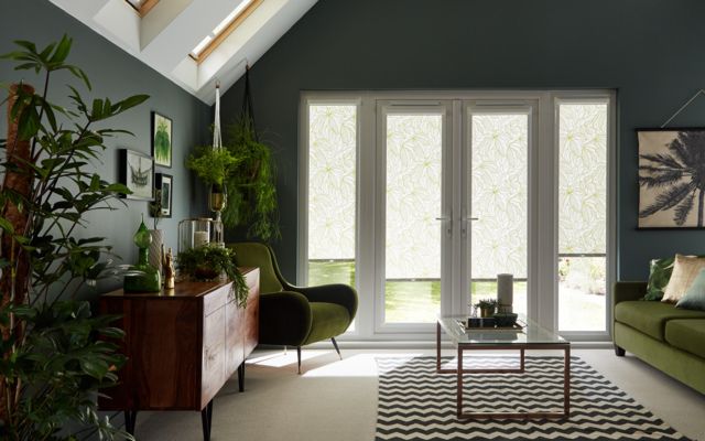 White roller blinds fitted to a door window in a living decorated in green and features potted plants