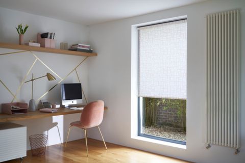 White roller blind fitted to a tall rectangular window in a study decorated with white walls