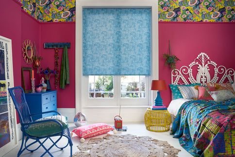 Colourful bohemian bedroom with hot pink walls and blue furniture with a blue pattern roller blind