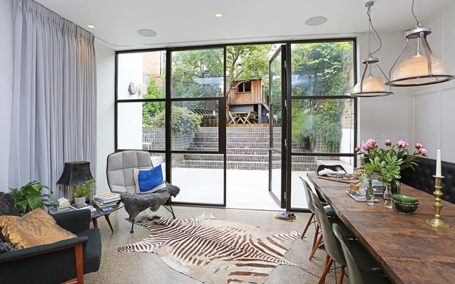 White pinch pleat curtains fitted to a wall in a dining room that opens out onto a patio and garden