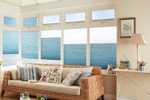 Blue coloured trillite blinds fitted to multiple windows in a room decorated in white with a sofa and table 