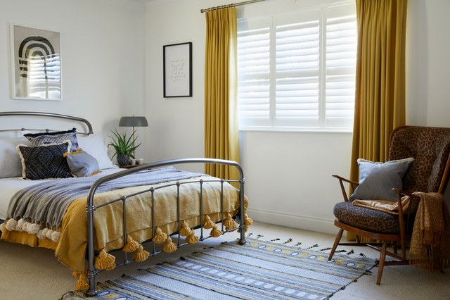 Bedroom with ochre curtains over white shutters