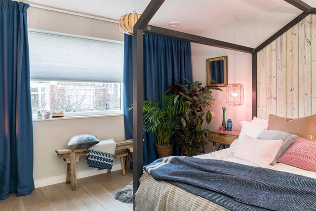 Blue curtains hanging over light blue pleated thermashade blinds in a cosy bedroom