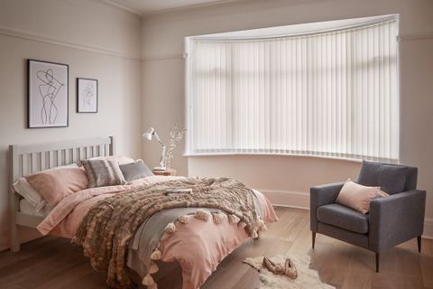 Minimal luxe bedroom with soft furnishings and a bow window dressed with light cream vertical blinds 