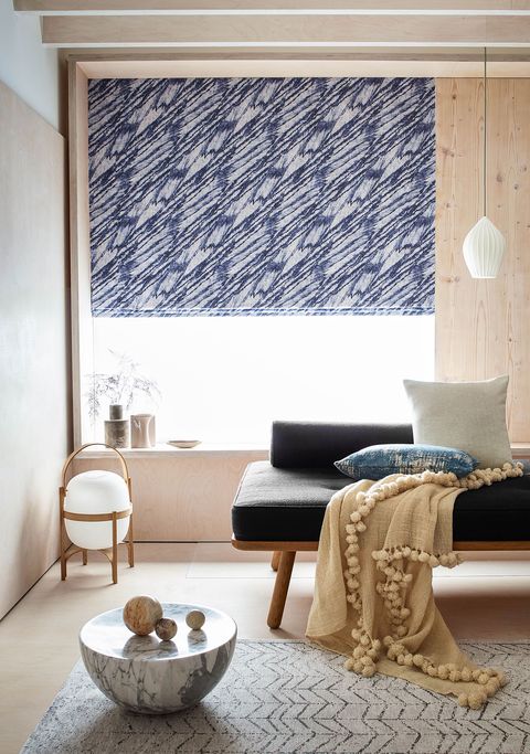 Blue patterned roman blinds hanging on a window in siting room, window is decorated with flower vases.