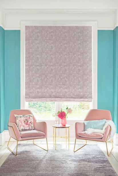 textured shimmering purple Roman blinds in living room. Light blue and printed cushions have been placed on two blush pink arm chairs with gold legs in the room