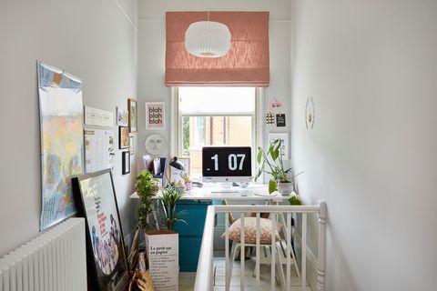 A white office space situated at the top of a staircase, with a pink blind in the window