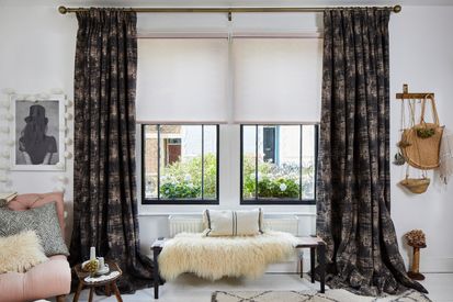 A white bedroom with two black sash windows dressing with dark curtains and light pink Roller blinds