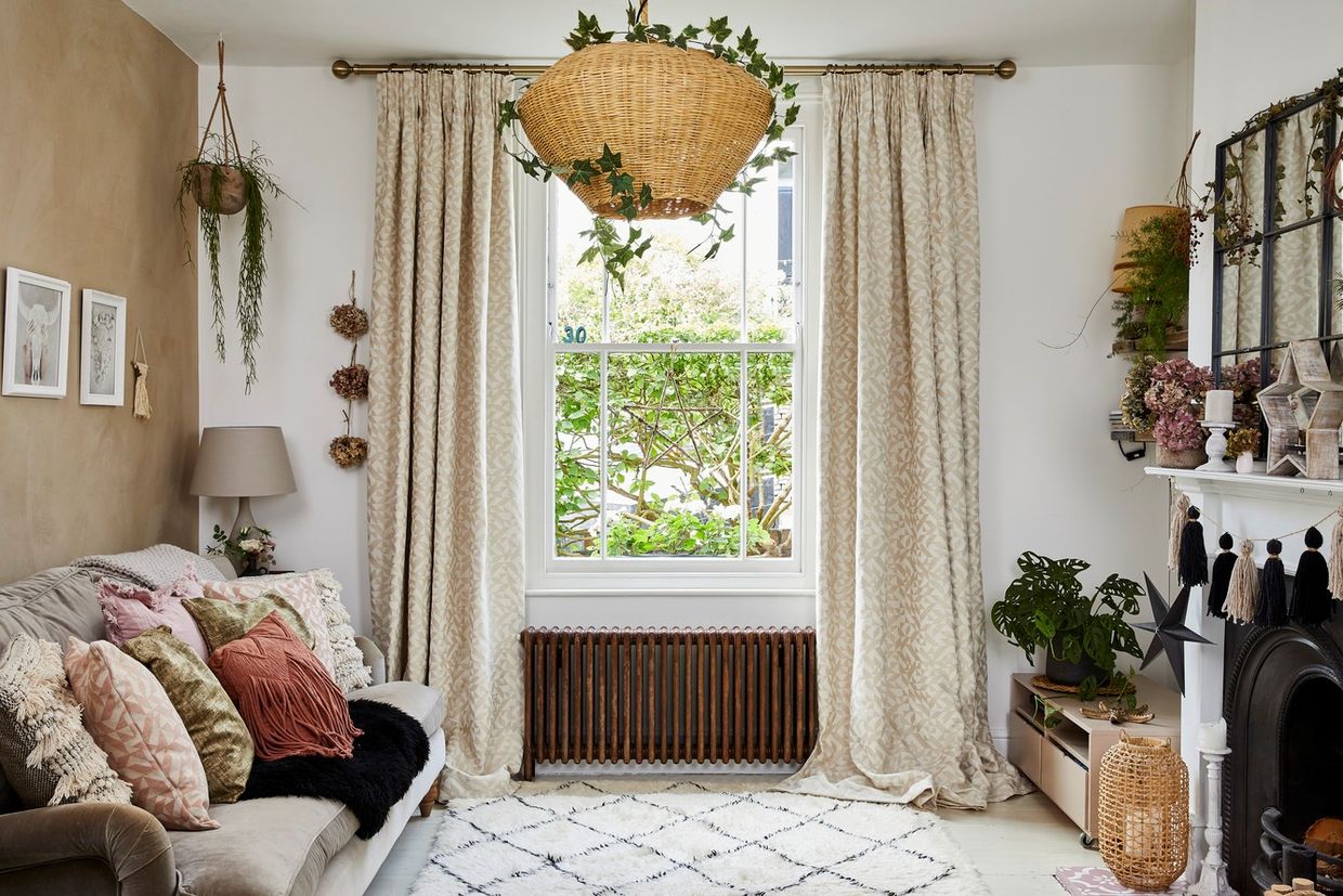 A living room with a single sash window dressed with beige coloured curtains