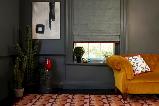 cley donkey roman blind with collette vixen fringing in a grey living room with an orange sofa and cactii