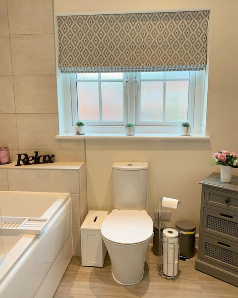 Cream roman blind featuring some diamond shape print hanging on window of bathroom
