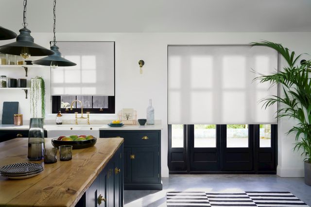 White coloured roller blinds fitted to a rectangular and bi fold door window in a dining room decorated in white and dark blue