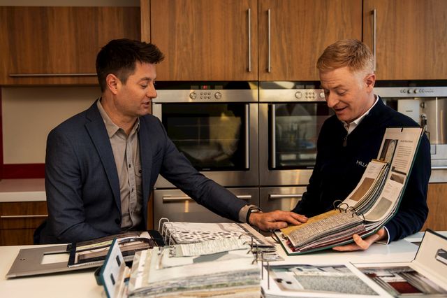 an advisor showing a customer a variety of fabric swatches in their kitchen