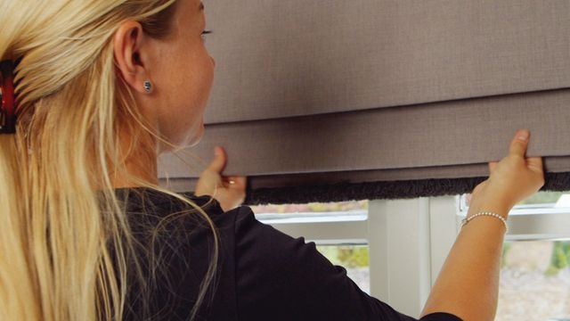 Close up of woman pulling down roman blind in grey with dark fringing