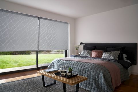 Blush pink bedroom with silver and grey patterned blinds over large sliding doors, next to kingsize bed with blush and grey accessories