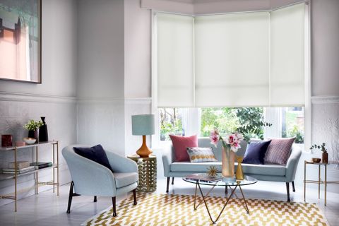 Grey living room with white bay-window blinds and warm, colourful furnishings