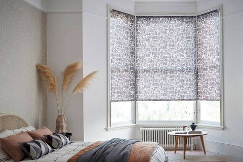 cosy bedroom with white and black patterned bay-window blinds and blush-pink and monochrome furnishings 