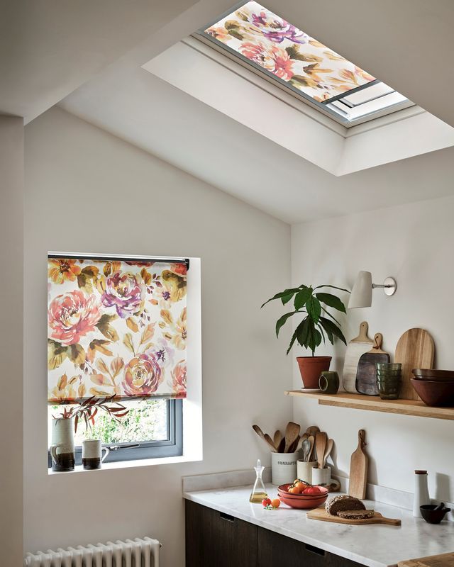 Two floral styled roller blinds, one fitted to a skylight window and another to a regular window in a white decorated kitchen